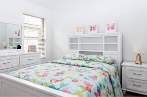Humble townhouse for rent - Pet-Friendly Apartments in Humble, TX - Edgewater at the Lagoon - Bedroom with a White-Framed Bed and Bright Bedding, Nightstand with Lamp, White Dresser with Drawers, and Window with White Blinds.