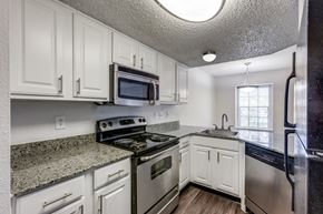 Austin apartment for rent - Austin, TX, Townhomes Near Q2 Stadium - Cottages at Wells Branch - Kitchen With White Cabinets, Granite Countertops, Stainless Steel Appliances, Ceiling Lights, and Wood-Style Floors.