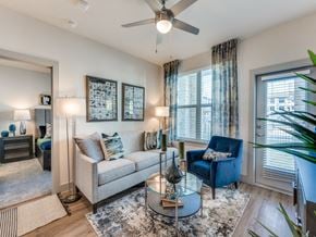 Saginaw apartment for rent - Luxury Apartments in Saginaw, TX, With In-Unit Washer And Dryer - Grand at Saginaw - Living Room With Sofa And Accent Chair, Glass Coffee Table, Ceiling Fan, And Balcony Door With Blinds.