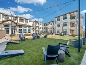 Saginaw apartment for rent - Pet-Friendly Luxury Apartments in Saginaw, TX - Grand at Saginaw - Courtyard Lawn With Adirondack Seating, String Lights Overhead, Cornhole Boards, And Surrounding Multi Story Apartment Buildings.