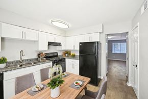 Marietta apartment for rent - Modern kitchen with white cabinets, black appliances, and dining table set for two.