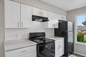 Fort Worth apartment for rent - A black refrigerator stands next to a stove in a kitchen with white cabinets.