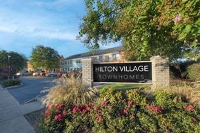 Newport News apartment for rent - The sign for Hilton Village Townhomes is surrounded by flowers and greenery.