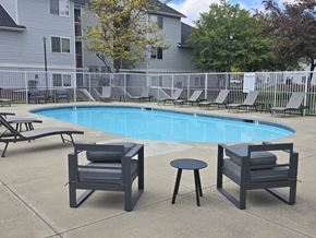 Coeur D Alene apartment for rent - Coeur d'Alene, ID, Apartments for Rent - Trail Lodge Apartments - Outdoor Swimming Pool With Sundeck, Lounge Chairs, Side Table, Patio Chairs, White Safety Fence, and Trees.
