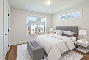 Asheville apartment for rent - Furnished bedroom with large window, a gray tufted bench, and a headboard against a white wall.