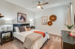 Waco apartment for rent - A bedroom with a bed, a ceiling fan, and a wall-mounted shelf with a plant on it.