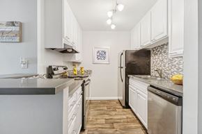 Downey apartment for rent - Downey, CA, Apartments - Park Regency Club Apartments - A Kitchen With White Cabinets, Gray Countertops, Stainless Steel Refrigerator And Dishwasher, Mosaic Tile Backsplash, And Wood Style Flooring.