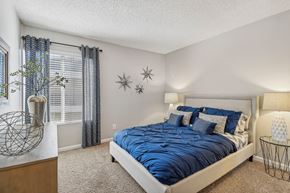 Downey apartment for rent - Pet-Friendly Apartments in Downey, CA - Park Regency Club Apartments - A Bedroom With Upholstered Bed, Blue Bedding, Matching Nightstands With Lamps, Carpet Flooring, And A Window.