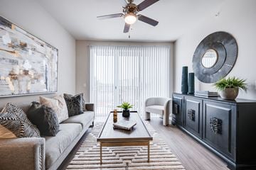Little Elm apartment for rent - A living room with a grey couch, a coffee table, a ceiling fan, and a large abstract painting on the wall.