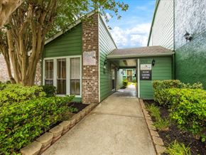 Houston apartment for rent - the entrance to a green building with a sidewalk and a tree