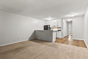 Macon apartment for rent - Element at 3900, Macon Apartments A kitchen with white cabinets and a black fridge is in the background of a living room with a beige carpet.