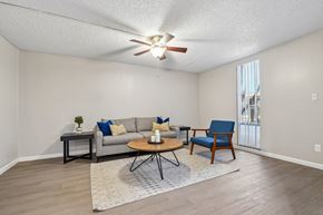 Tempe apartment for rent - A living room with a grey couch, a blue chair, and a ceiling fan.
