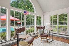 Duluth apartment for rent - A room with a chair and a table in front of a window with a view of a pool and trees.