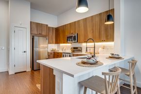 Dallas apartment for rent - 2-Bedroom Apartments in Old East Dallas, TX - 4600 Ross - Kitchen With White Quartz Island, Wood Cabinets, Stainless Steel Appliances, Matte Black Faucet, And Pendant Lights.