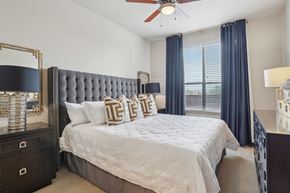 Houston apartment for rent - A bedroom with a large bed, a ceiling fan, and a window with blue curtains.