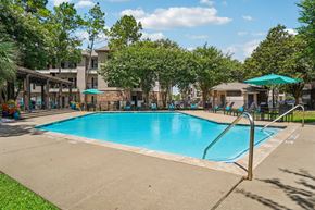Houston apartment for rent - A large swimming pool surrounded by trees and a building in the background.