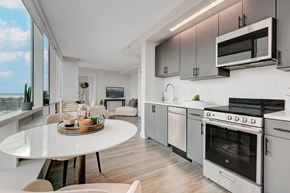 New Rochelle apartment for rent - A modern kitchen with a white table and chairs, a microwave above the stove, and a view of the ocean through the window.