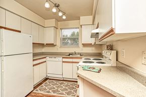 University Place apartment for rent - Dog-Friendly Garden-Style Apartments in University Place, WA - Carriage House - Kitchen with Wood-Style Flooring, Custom Cabinetry, Light Fixtures, 4-Burner Range, Range Hood, Refrigerator, and Dishwasher.
