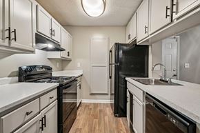 Duluth apartment for rent - A black refrigerator stands in a kitchen with white cabinets and a wooden floor.