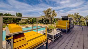 Aurora apartment for rent - Aurora, CO apartments - Aurora Hills - a poolside deck with yellow chairs, a table, and a railing overlooking a blue pool and various types of trees.