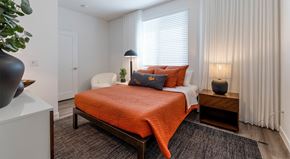 Phoenix apartment for rent - A bedroom with a bed covered in an orange blanket and a white chair.