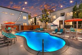 Colton apartment for rent - Apartments for Rent in Colton, CA - Ardella at Reche Canyon - Swimming Pool Features Glowing Blue Water, Lounge Chairs, Patio Tables With Red Umbrellas, And String Lights Overhead.