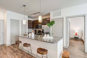 Nashville apartment for rent - Apartment kitchen with granite countertop island, wooden stools, stainless steel appliances, and view into bedroom.