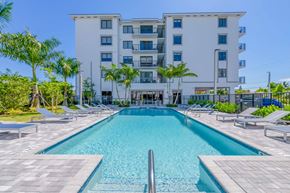 Miami apartment for rent - Apartment building with a swimming pool, lounge chairs, and palm trees on a sunny day.