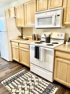 Spokane apartment for rent - Spokane, WA Apartments for Rent - Deer Creek - Kitchen with Plank Flooring, Rug, White Appliances, and Wood-Tone Cabinetry.