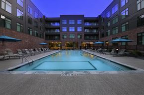 College Station apartment for rent - A swimming pool in a courtyard surrounded by chairs and umbrellas.