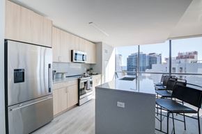 New Rochelle apartment for rent - A modern kitchen features light wood cabinets, stainless steel appliances, a large marble-topped island, and floor-to-ceiling windows with a bright city view.