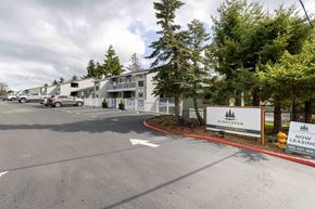 Lynnwood apartment for rent - Lynnwood, WA, Apartments - Evergreen Grove - Parking Lot with Vehicles, Trees, Fence, Apartment Buildings, and Property Signage.