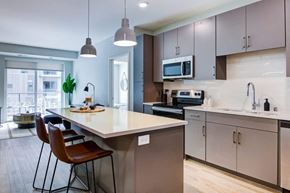Bloomington apartment for rent - Bloomington, MN, Luxury Apartments with In-Unit Washer and Dryer - The Fenley - Kitchen with Quartz Island Seating, Pendant Lights, Gray Cabinets, and Stainless Steel Appliances.