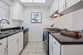 Hayward apartment for rent - 1-Bedroom Apartments in Hayward, CA - Glen Oaks Apartments - Bright Galley Kitchen With White Cabinets, Dark Countertops, Dishwasher, Gas Range, and Tile Flooring Beneath Skylight.