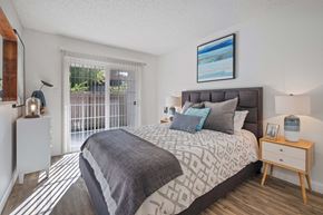 Hayward apartment for rent - One Bedroom Apartments in Hayward CA - Glen Oaks - Spacious Bedroom with Wood-Style Flooring, a Bed, Wooden Nightstands with Lamps, White Dresser, and Large Window/Sliding Door with Patio Access
