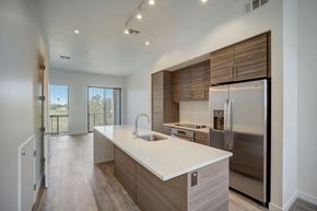 Scottsdale apartment for rent - 2-Bedroom Apartments in Scottsdale, AZ - Dusk Scottsdale - Gourmet Kitchen with Wood-Style Flooring, Stainless Steel Appliances, White Quartz Countertops, Cooking Island, Modern Custom-Wood Cabinetry, Overhead Lighting, and View of Living Room.