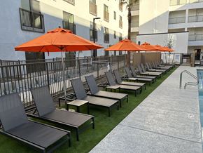 Phoenix apartment for rent - Studio Apartments in Downtown Phoenix, AZ - VB on 12th Street - Poolside Lounge Seating with Orange Umbrellas on a Patch of Artificial Grass Turf and Surrounded by a Fence.