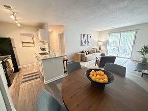 Greensboro apartment for rent - A kitchen area with a refrigerator, a dining table with chairs, and a bowl of oranges on the table.