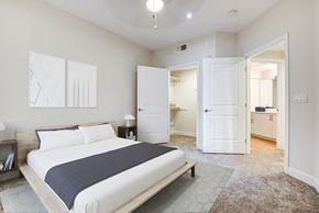 Milpitas apartment for rent - 1-Bedroom Apartments in Milpitas, CA - Ilara Apartments - Bedroom With White Bedding, Dark Throw Blanket, Open Closet, Ceiling Fan, Nightstands, Wall Art, Carpeted Flooring, And Bathroom Access.