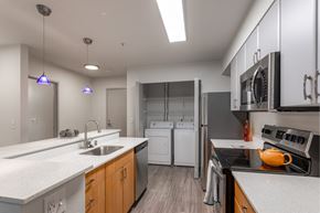 Seattle apartment for rent - Apartments In Fremont For Rent - Epicenter - A Modern Open-Concept Kitchen With Light Wood Lower Cabinets, White Upper Cabinets, And A Laundry Closet In The Background.