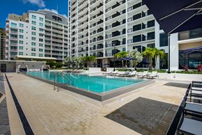 Miami apartment for rent - One-Bedroom Apartments in Miami, FL - MB Station - Sparkling Swimming Pool Surrounded by Lounge Seating, Palm Trees, Raised Planters, and an Apartment Building in the Background.
