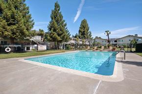 Gilroy apartment for rent - Apartment Gilroy, CA - Mission Park - Gated Sparkling Pool with Tan Lounge Chairs, Grassy Lawn, Trees, and View of Apartment Buildings in the Background.