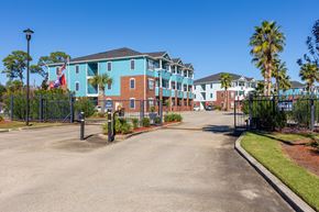 Biloxi apartment for rent - A large building with a blue and red facade is surrounded by a black fence.