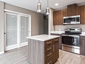 Seattle apartment for rent - Seattle, WA Apartments Near University Village - Origin - Kitchen With Contemporary Wood Finish Flooring, Stainless Steel Appliances, Wood-Tone Flat-Panel Cabinets, Stone Countertops, Kitchen Island, And Pendant Lights.