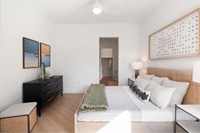 Houston apartment for rent - Downtown Houston, TX, Apartments with In-Unit Washer and Dryer - The Laura - Bedroom With A Woven Headboard Bed, White Bedding And Green Throw, Matching Nightstand Lamps, and Black Dresser.