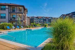 Bentonville apartment for rent - Pet-Friendly Rentals in Bentonville, AR – Parc at Bentonville – A large swimming pool with the apartments surrounding it and beach chairs