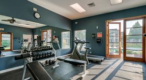 Coeur D Alene apartment for rent - Coeur d'Alene, ID, Apartments - Rockwood Lodge - Fitness Center with Rubber Matting, Large Mirror, Dumbbells, Cardio Equipment, Ceiling Fan, Recessed Lighting, and a Doorway Leading to the Pool Area.