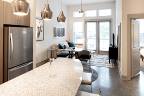 Dallas apartment for rent - A modern kitchen with a refrigerator, a dining table with chairs, and pendant lights hanging from the ceiling.