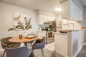 Glendale apartment for rent - Apartments Near Westgate, Glendale, AZ - Ardella on 67th - Kitchen with Open Space to Dining Area, Featuring Stainless Steel Appliances, White Cabinetry, a Table, and Chairs.