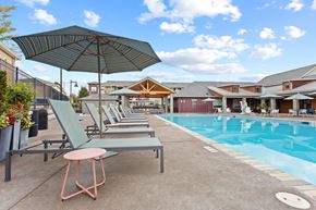 Tigard apartment for rent - A poolside area with lounge chairs and an umbrella.